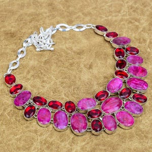 Puede incluir: Un collar de plata con piedras preciosas ovaladas y redondas en tonos rojos y magenta. Las piedras están engastadas en plata y dispuestas en un patrón curvo.
