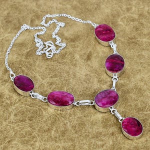 Op de afbeelding: Een zilveren ketting met ovale, dieproze edelstenen. De edelstenen zijn gezet in zilveren zettingen en verbonden door zilveren schakels, wat een elegant sieraad creëert. De ketting heeft een fijne ketting.