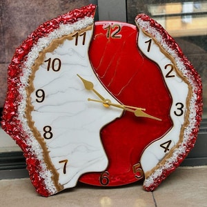 May include: A wall clock with an irregular, geode-inspired shape featuring a deep red center and a white marbled section. The clock face has gold-colored numerals from 1 to 12 and matching gold-colored hour, minute, and second hands. The outer edge is textured with a combination of red and white crystalline details.