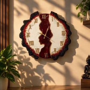 May include: A round wall clock featuring a white marble-effect face divided by a central vertical band of deep red resin. The clock has gold Roman numerals and gold hands, surrounded by a textured, jagged black and red outer border.