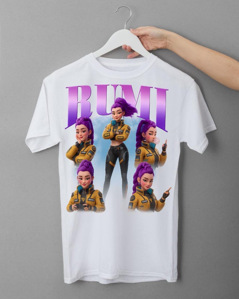 May include: White t-shirt featuring the name "RUMI" in purple and a graphic of a character with purple hair and a yellow jacket. The character is shown in multiple poses. The shirt is hanging on a white hanger.
