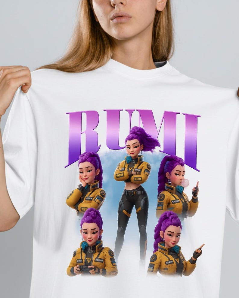 May include: White t-shirt featuring the word "RUMI" in purple block letters above a graphic of a woman with purple hair in a yellow jacket and black pants. The graphic includes multiple poses of the woman.