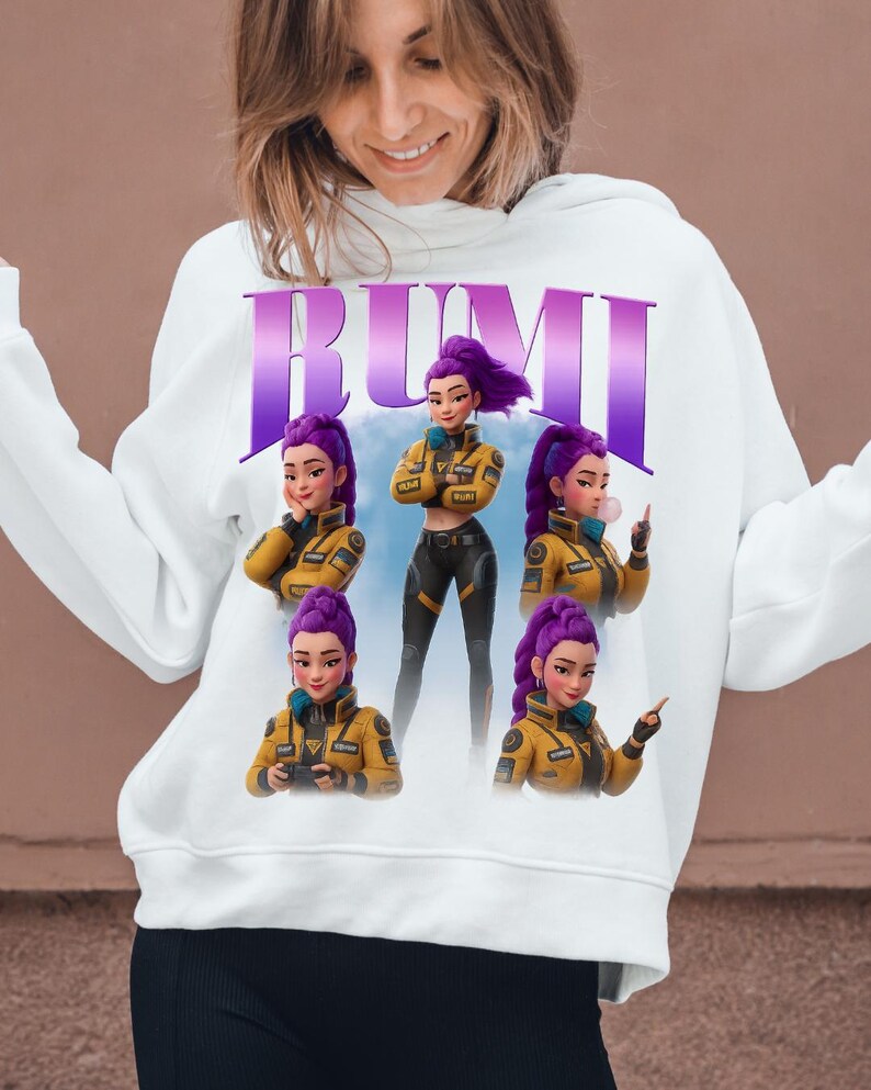 May include: White hoodie featuring the word "RUMI" in purple letters. The graphic design includes a cartoon character with purple hair in a yellow jacket and black pants. The character is shown in multiple poses.