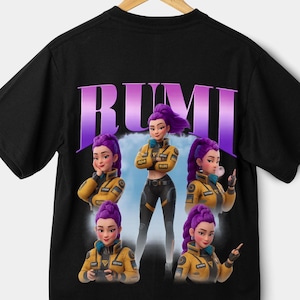 May include: Black t-shirt featuring a graphic of a character with purple hair and a yellow jacket. The word "RUMI" is printed in purple above the character. The character is shown in multiple poses.