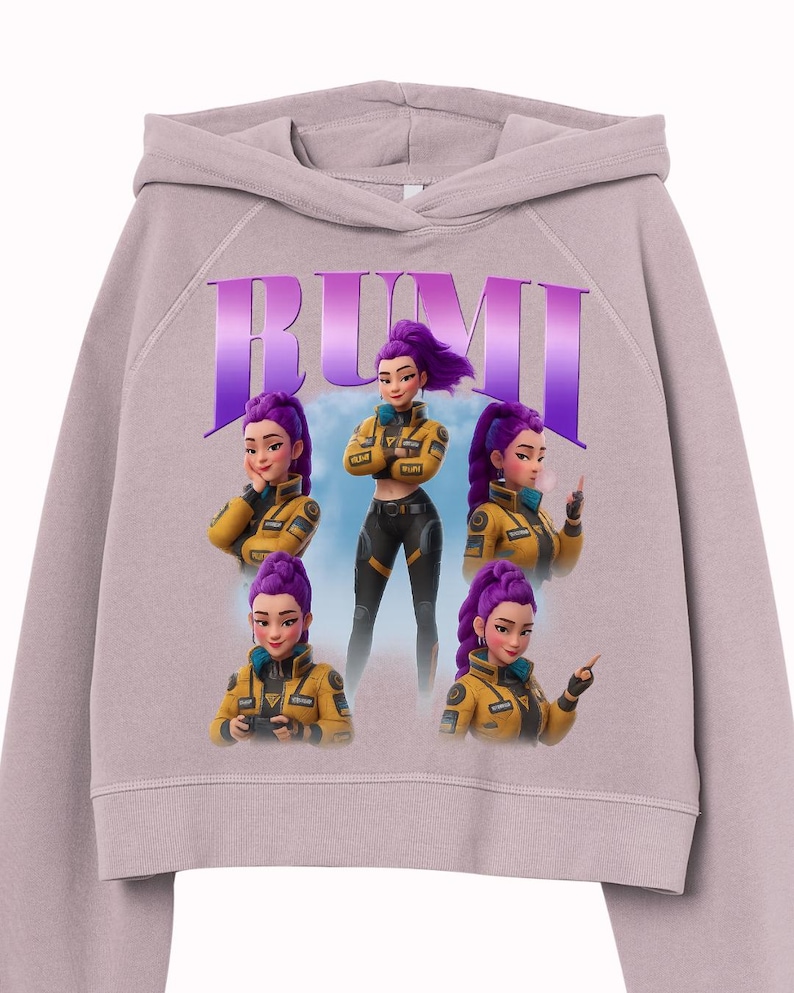May include: A light purple cropped hoodie featuring a graphic of a woman with purple hair in a yellow jacket. The word "RUMI" is printed in large purple letters above the graphic. The graphic shows the woman in different poses.