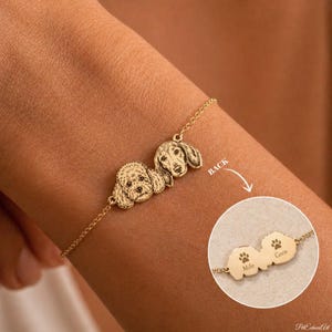 May include: A gold-toned chain bracelet featuring two engraved dog portraits. An inset shows the reverse side of the charms, which displays two paw prints and the engraved names Milo and Coco. The bracelet is displayed on a wrist.