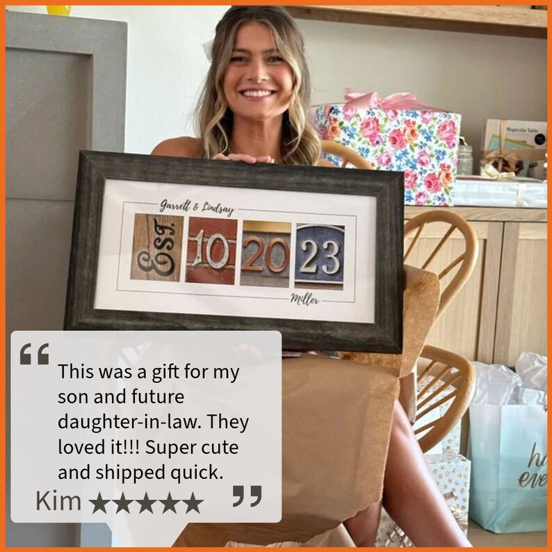May include: A framed print with a personalized design featuring the names "Garrett & Lindsay" and the dates "EST 10 20 23" with the word "Miller" below. The print is in a dark wood frame and is being held by a person.
