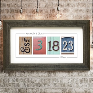 May include: A framed print with a personalized message for Amanda & Chase. The print features a collage of vintage house numbers, including the letters "EST" and the numbers "3", "18", and "23". The print is signed "Hillman".