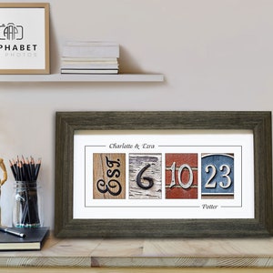 May include: A framed print with a rustic wood background featuring the names Charlotte & Ezra and the last name Potter. The names are spelled out using vintage-style house numbers.