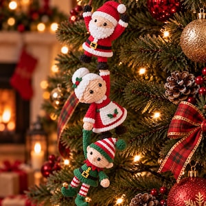 May include: A vertical chain of three crocheted ornaments hanging from a brown cord. The top figure is Santa Claus in a red suit, the middle is a woman with white hair in a red dress and white apron, and the bottom is an elf in green and red.