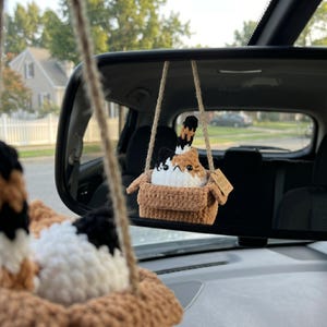 Pu&ograve; includere: Un peluche di gatto calico all'uncinetto seduto dentro una scatola marrone all'uncinetto, sospeso da uno spago di juta. Il gatto ha macchie di lana bianca, nera e arancione, occhi di sicurezza neri e un cartellino marrone sul lato.