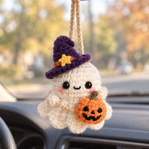 May include: A crocheted ghost ornament hanging from a beige cord, featuring a purple witch hat with a yellow star, black bead eyes, pink cheeks, and a small orange jack-o'-lantern pumpkin held in its arms, crafted with white yarn.