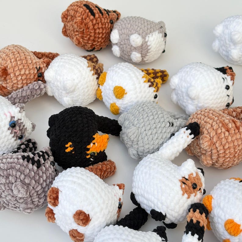 Puede incluir: Una colecci&oacute;n de juguetes para gatos hechos a mano con ganchillo en varios colores. Los juguetes presentan detalles en blanco, marr&oacute;n, negro, gris y naranja. Algunos tienen manchas, rayas o parches. Los juguetes son suaves y afelpados, con ojos y narices negros.