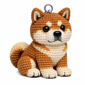 Può includere: Figurina di cane Shiba Inu all'uncinetto nei toni del marrone e crema, con occhi e naso neri. Il peluche fatto a mano ha un anello portachiavi attaccato alla testa. Il cane è seduto con la coda arricciata.