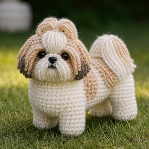 May include: A crocheted Shih Tzu dog figurine in cream and tan. The handmade dog has a fluffy tail and head, with dark eyes and a small black nose. The dog is standing on green grass.