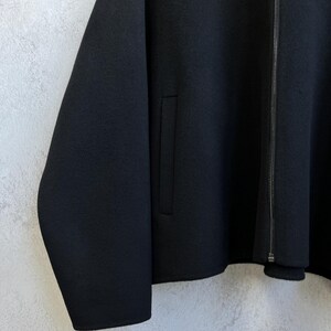 Pode incluir: Casaco preto com fecho de correr e um bolso. O casaco tem mangas compridas e um design minimalista. O tecido parece ser um material liso e mate.