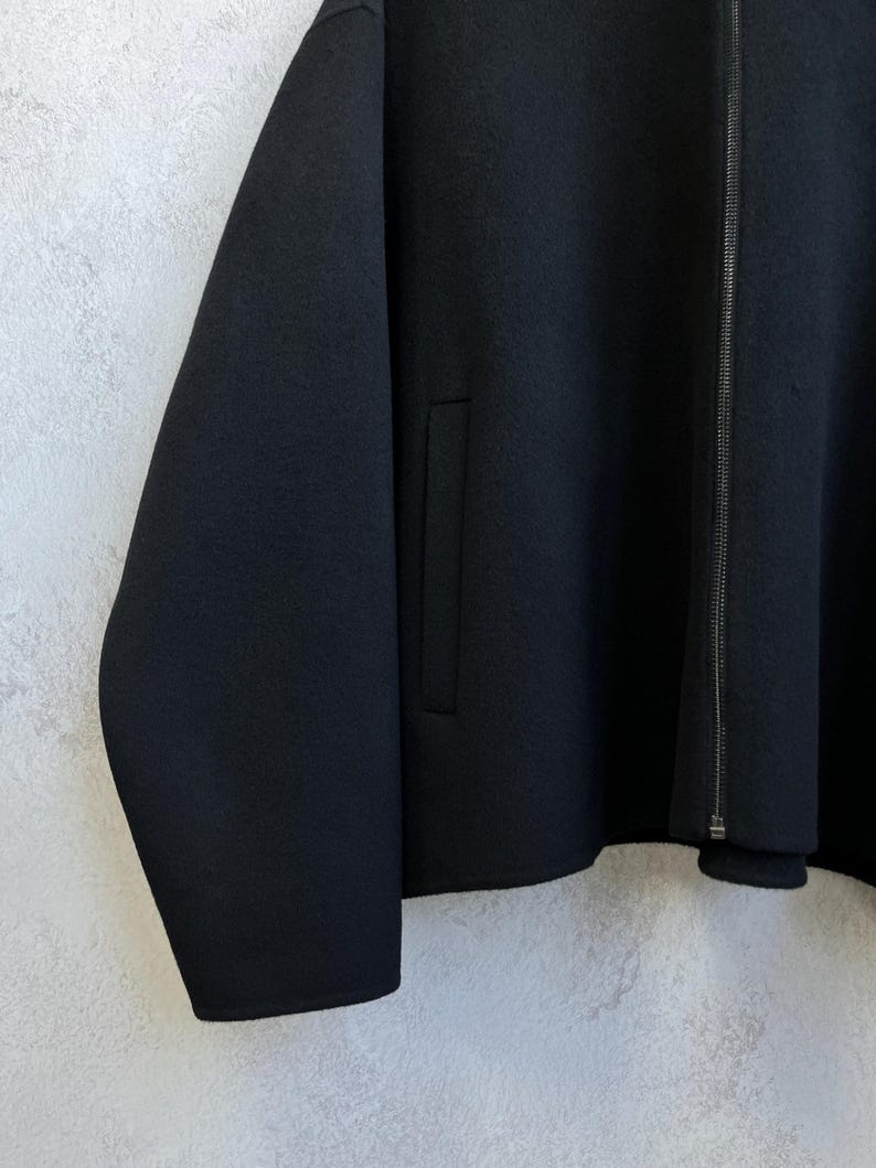 Pode incluir: Casaco preto com fecho de correr e um bolso. O casaco tem mangas compridas e um design minimalista. O tecido parece ser um material liso e mate.