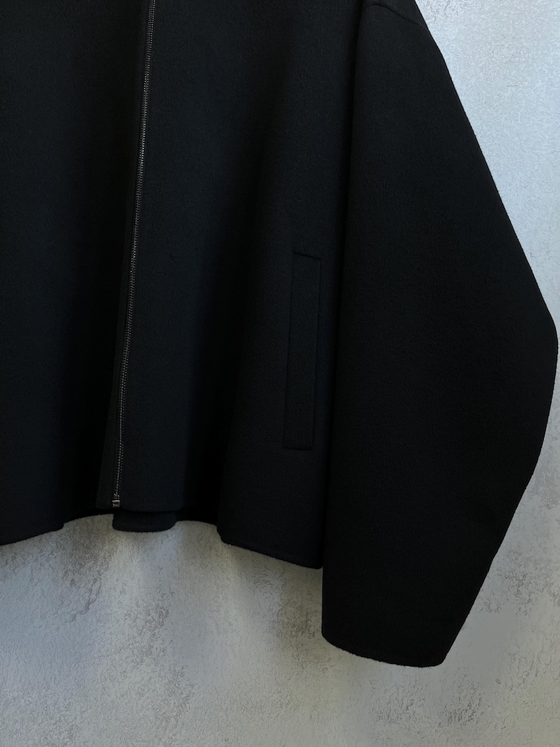 Pode incluir: Casaco preto com fecho de correr e um bolso. O casaco tem um design simples e minimalista, com um corte ligeiramente folgado. O tecido parece ser um material macio e tecido.