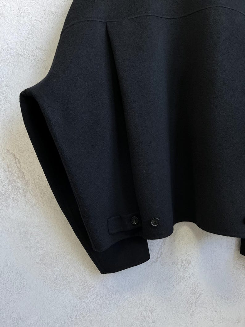 Pode incluir: Uma caneca de cer&acirc;mica branca com uma al&ccedil;a preta e o texto "But First, Coffee" em negrito preto. A caneca est&aacute; sobre um fundo desfocado, sugerindo um ambiente acolhedor.