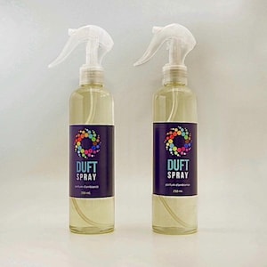 Peut inclure: Deux flacons pulvérisateurs transparents remplis d'un liquide jaune clair. Chaque flacon est doté d'un pulvérisateur blanc et d'une étiquette violet foncé avec le texte "DUFT SPRAY" et un motif circulaire coloré. Les flacons sont étiquetés "250 ml".