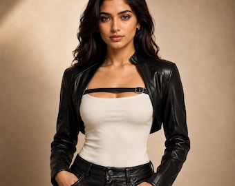 May include: A black leather bolero jacket with a high collar and long sleeves. The jacket is worn over a white tank top. The model is wearing black leather pants. The jacket has a black strap with a silver buckle.