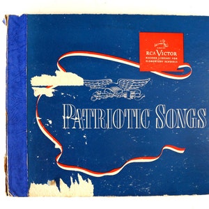 Puede incluir: Un libro azul con un diseño de cinta roja, blanca y azul. El libro tiene el título "PATRIOTIC SONGS" y un logotipo de RCA Victor Record Library for Elementary Schools.