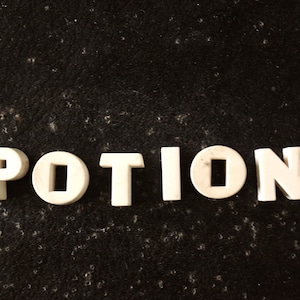 Puede incluir: Letras de plástico blanco deletreando la palabra "POTIONS" sobre un fondo negro.