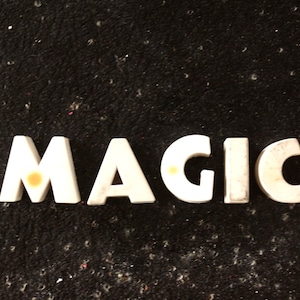 Puede incluir: Letras de plástico blanco deletreando la palabra "MAGIC" sobre un fondo negro.