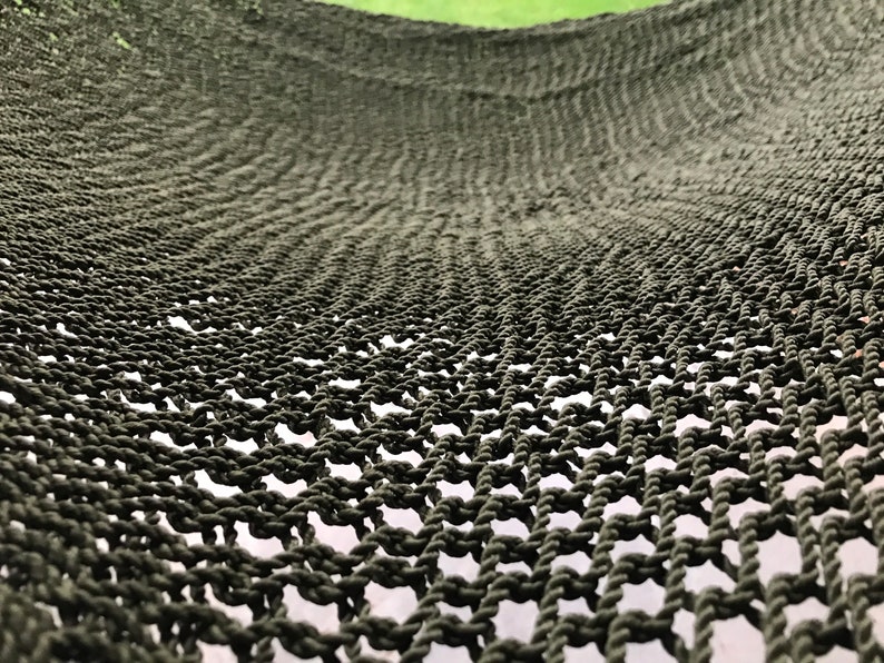 May include: Close-up of a dark green hammock made of woven rope. The hammock is hanging and the weave pattern is visible.