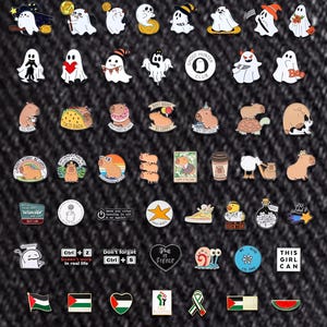 May include: A selection of enamel pins with diverse designs, such as ghosts, capybaras, and motivational phrases. Some pins display text like "Ghost Hunter Club," "Taco Bada," and "This Girl Can." The pins are set against a dark denim background.