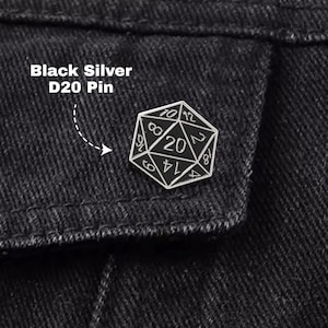 May include: A black and silver D20 pin, a twenty-sided die, is pinned to black denim. The pin has a silver outline with black numbers and is labeled "Black Silver D20 Pin". This pin is a perfect accessory for tabletop gaming enthusiasts.