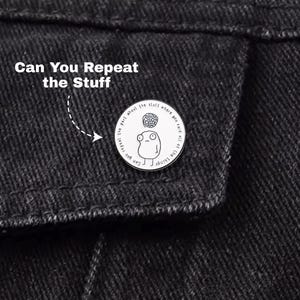 May include: A black denim jacket with a white pin. The pin features a cartoon character and the text "Can You Repeat the Stuff". The pin is round and has a black and white design.