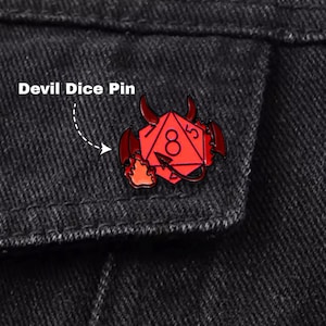 May include: A red devil dice pin with black accents, featuring a number 8 on the die. The pin is attached to a black denim jacket. The text "Devil Dice Pin" is above the pin.