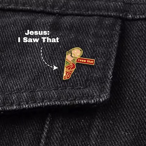 May include: A gold-coloured enamel pin depicting Jesus with the text "I saw that." The pin is set against a dark denim background, with the text "Jesus: I Saw That" above it.