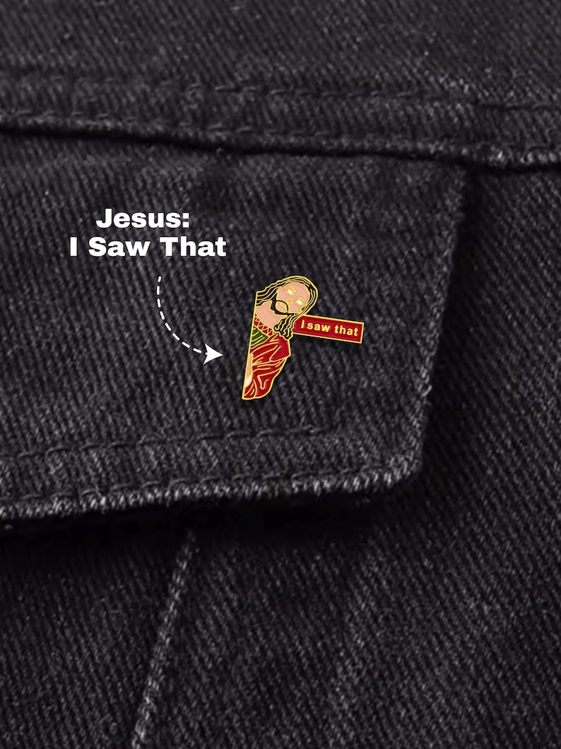 May include: A gold-coloured enamel pin depicting Jesus with the text "I saw that." The pin is set against a dark denim background, with the text "Jesus: I Saw That" above it.