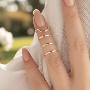 Può includere: Anelli d'oro per dita in vari design. Gli anelli sono indossati sulle dita, con un anello curvo in alto e altri tre anelli sotto. Gli anelli sono semplici ed eleganti, adatti per l'uso quotidiano o per occasioni speciali.