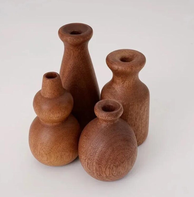 May include: Four handcrafted wooden vases in varying shapes and sizes. The vases are made of a warm brown wood and have a smooth, natural finish. The collection includes a gourd-shaped vase, a tall conical vase, and two others.