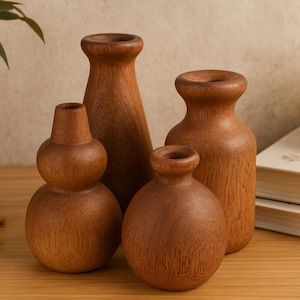 May include: Four wooden vases of varying shapes and sizes are arranged on a wooden surface. The vases are a warm brown color, with a natural wood grain visible. A candle and books are in the background, suggesting a decorative theme.