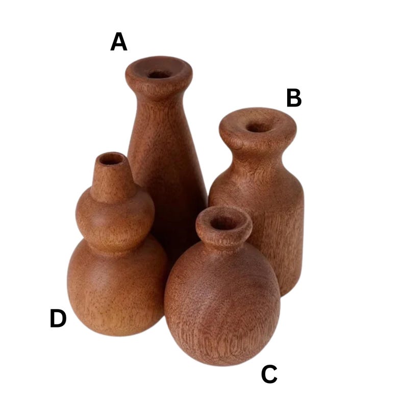 May include: Four small, handcrafted wooden vases in varying shapes. The vases are made of a reddish-brown wood and have a smooth, natural finish. The shapes include a tall, conical vase, a rounded vase, and two other unique designs.