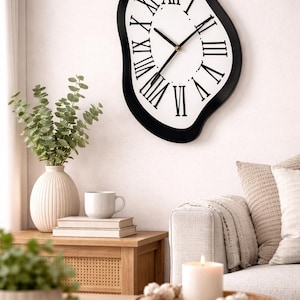 Puede incluir: Un reloj de pared único con un marco negro ondulado y una esfera blanca. El reloj presenta números romanos y manecillas negras, creando un diseño artístico moderno. El reloj está montado en una pared blanca, en un interior de tonos neutros.