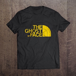 May include: Black t-shirt featuring the text "THE GHOST FACE" in yellow and black, designed in a style similar to a well-known outdoor brand. The shirt is made of a soft fabric and is suitable for everyday wear. The design is eye-catching.
