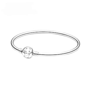 May include: A polished silver bangle bracelet featuring a single spherical charm. The charm is engraved with a celestial constellation pattern consisting of small stars and lines, with a single clear stone set into one of the star shapes.