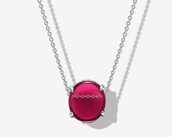 May include: A silver chain necklace featuring a round, polished, deep magenta-colored gemstone pendant held in place by four silver prongs. The smooth, reflective surface of the stone shows a subtle reflection of the chain links.