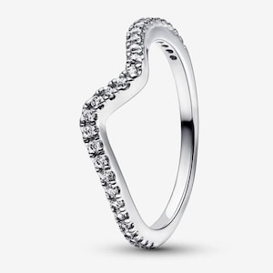 May include: A silver-coloured ring featuring a curved, V-shaped band design. The outer surface of the band is set with a continuous row of small, clear, round-cut stones that follow the contour of the wave shape, creating a sparkling, metallic finish.