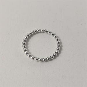 Peut inclure: Une bague fine et circulaire en métal argenté poli, composée d'une bande continue de petites perles sphériques uniformes disposées côte à côte pour créer un aspect texturé et perlé sur toute la circonférence de la bague.