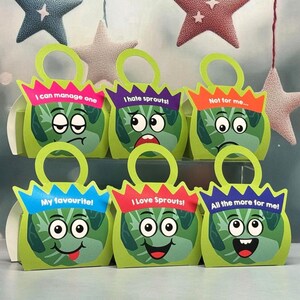 May include: Six green paper gift bags with handles, each featuring a cartoon Brussels sprout character with a unique facial expression and text: I can manage one, I hate sprouts!, Not for me..., My favourite!, I Love Sprouts!, and All the more for me!
