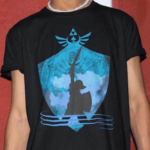 May include: Black t-shirt featuring a blue and white graphic design. The design includes a shield, a sword, and a silhouette of a figure. The shirt is made of a soft material.