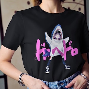 May include: Black t-shirt featuring a cartoon illustration of a person in a shark costume. The design includes pink Japanese text and is paired with blue jeans and sneakers. The shirt is a casual wear item.