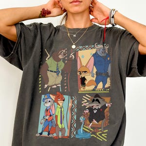 Puede incluir: Camiseta Comfort Colors gris oscuro con un gr&aacute;fico colorido de personajes de Zootopia. El dise&ntilde;o incluye im&aacute;genes de un perezoso, un zorro, un conejo y otros personajes. La camiseta tiene mangas cortas y cuello redondo.