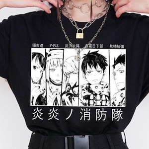 May include: Black t-shirt with a manga-style illustration of characters and Japanese text. The outfit includes black cargo trousers and a silver chain belt. The model is also wearing layered silver necklaces and a padlock pendant.